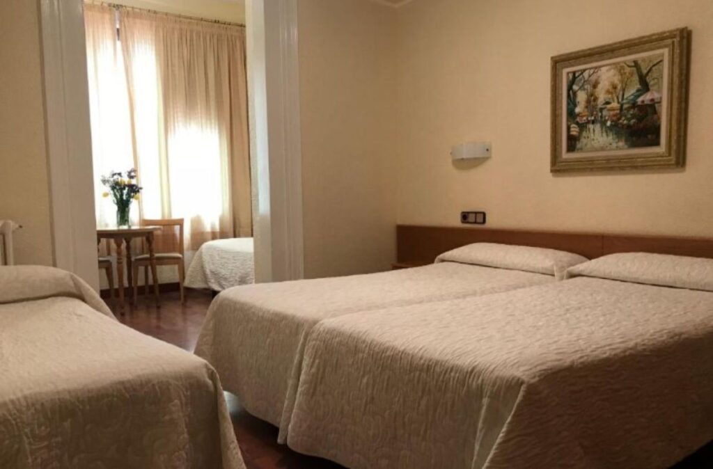 Classic triple room with cream quilted bedspreads, dark hardwood floors, framed landscape painting and window seating