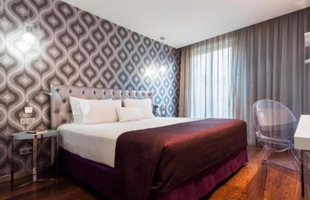 Retro-styled double room with floor-to-ceiling geometric patterned wallpaper, tufted headboard and hardwood floors