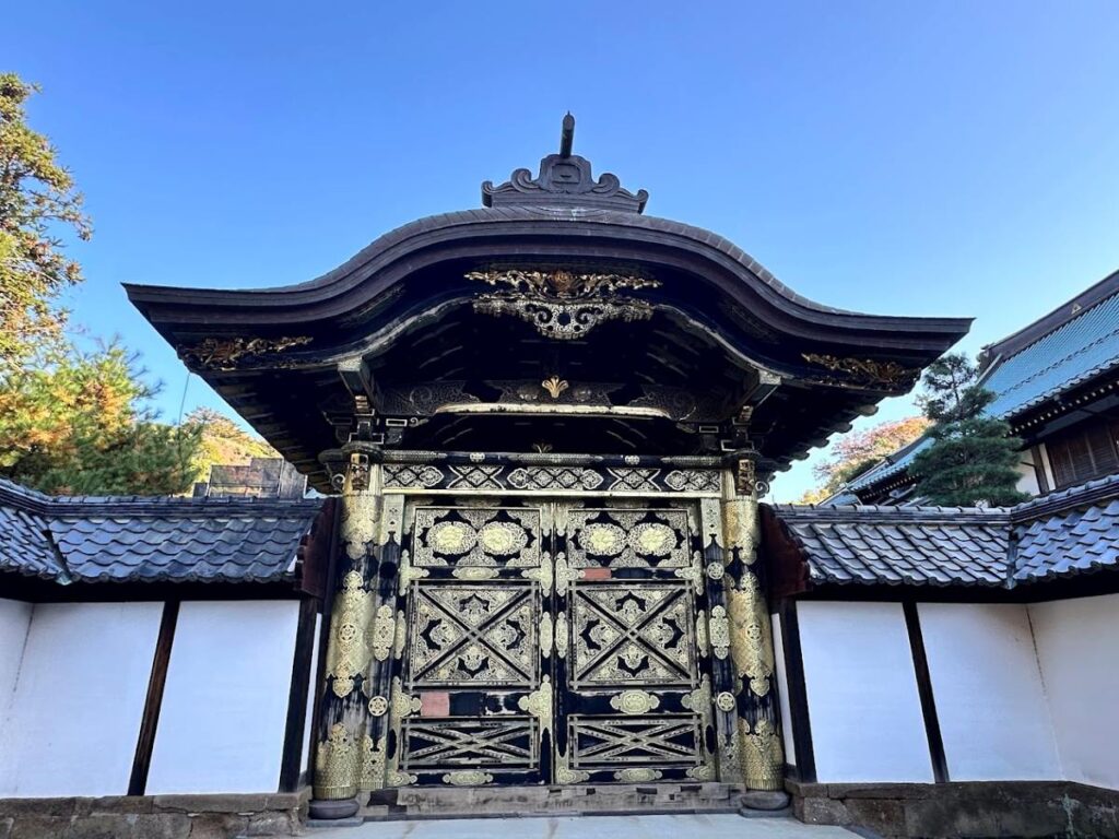 Ornate temple gate with gold detailing and curved roof, set against a vivid blue sky.