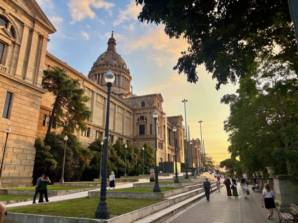 MNAC exterior at golden hour, with the domed museum façade, lampposts and people walking along Montjuïc.