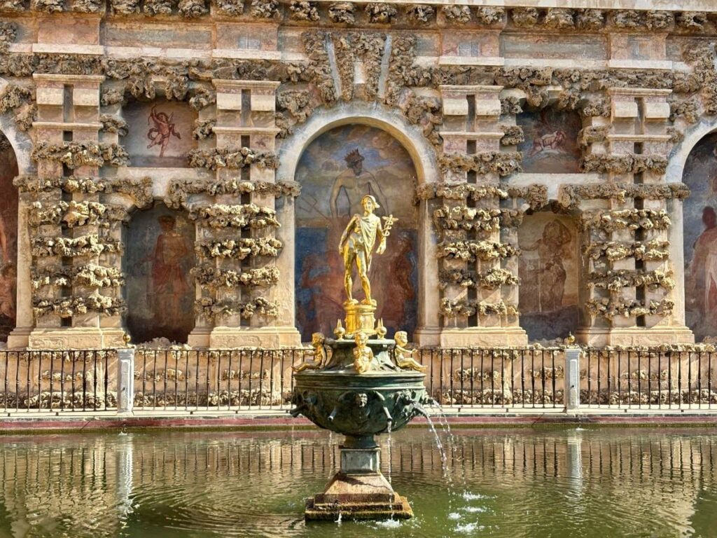 Mercury fountain in the Royal Alcázar, circular pool in front of a rusticated wall with arches, frescoes and stonework.