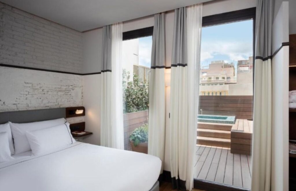 Contemporary double room with whitewashed brick wall, sheer curtains and private timber terrace with plunge pool