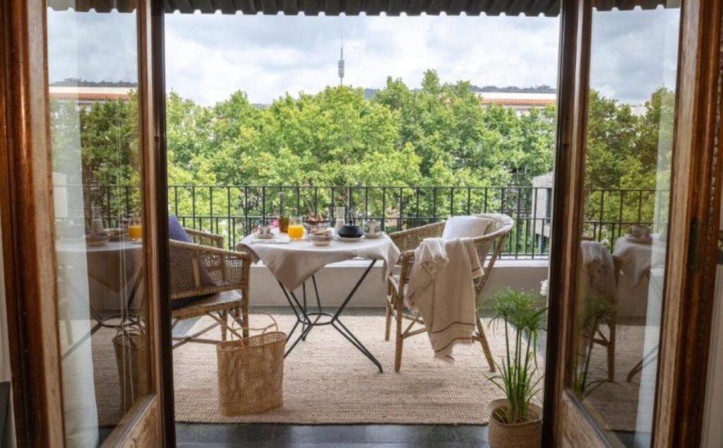 Private balcony breakfast table with rattan chairs, orange juice and tree-lined views towards a communications tower