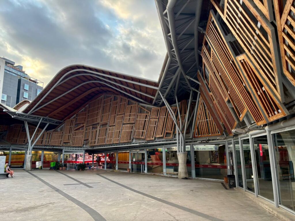 Curved wooden roof and timber shutters of Santa Caterina Market, with steel beams and an open plaza.