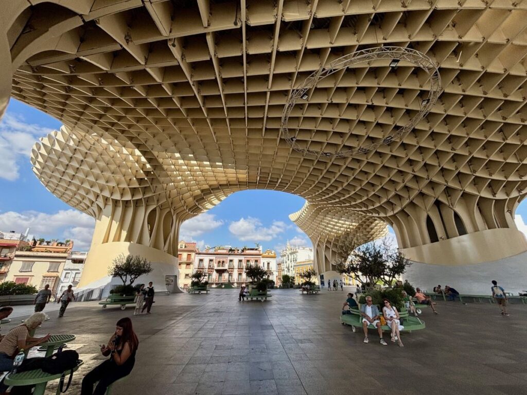 Under Metropol Parasol in daylight, honeycomb canopy overhead with people sitting on benches.