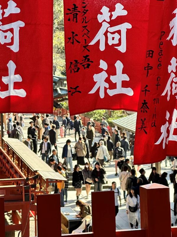 Crowds walking through a shrine approach, framed by red hanging banners with bold Japanese characters.