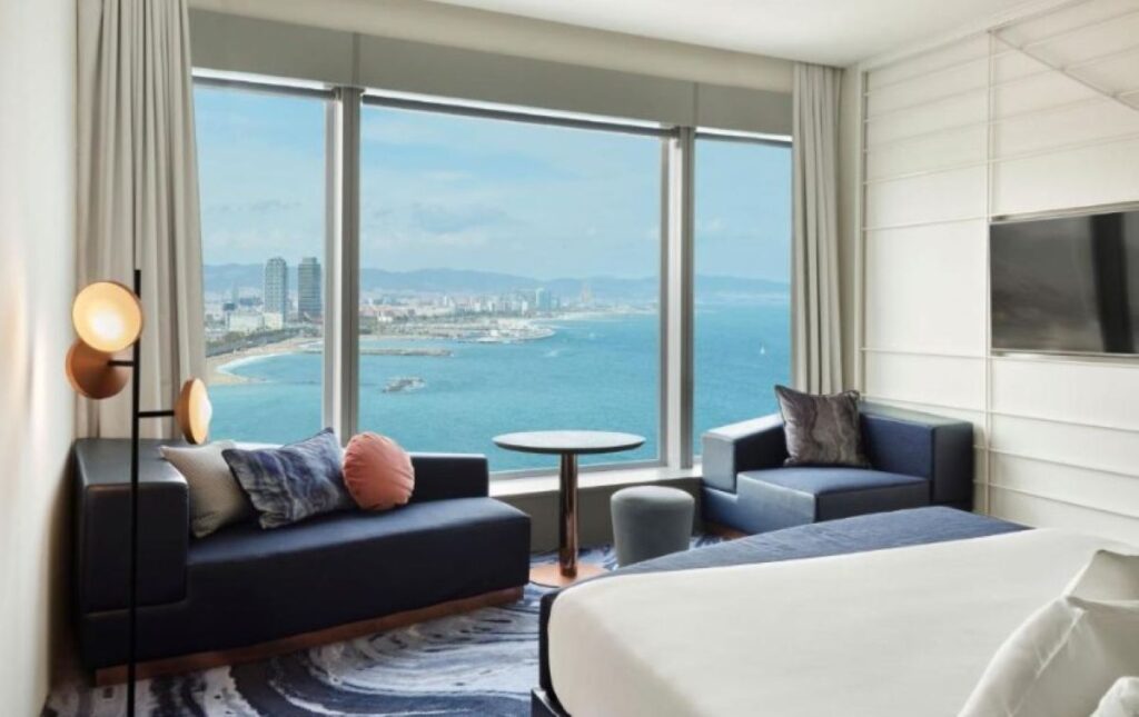 Stylish suite with navy seating, floor-to-ceiling windows and sweeping views over the Mediterranean beach and coastline