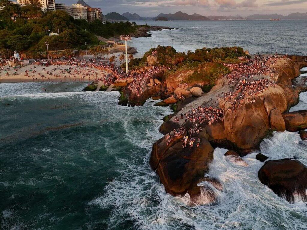Crowds gathered on Arpoador Rock at sunset, waves crashing below, Devil's Beach and the Atlantic stretching to the horizon