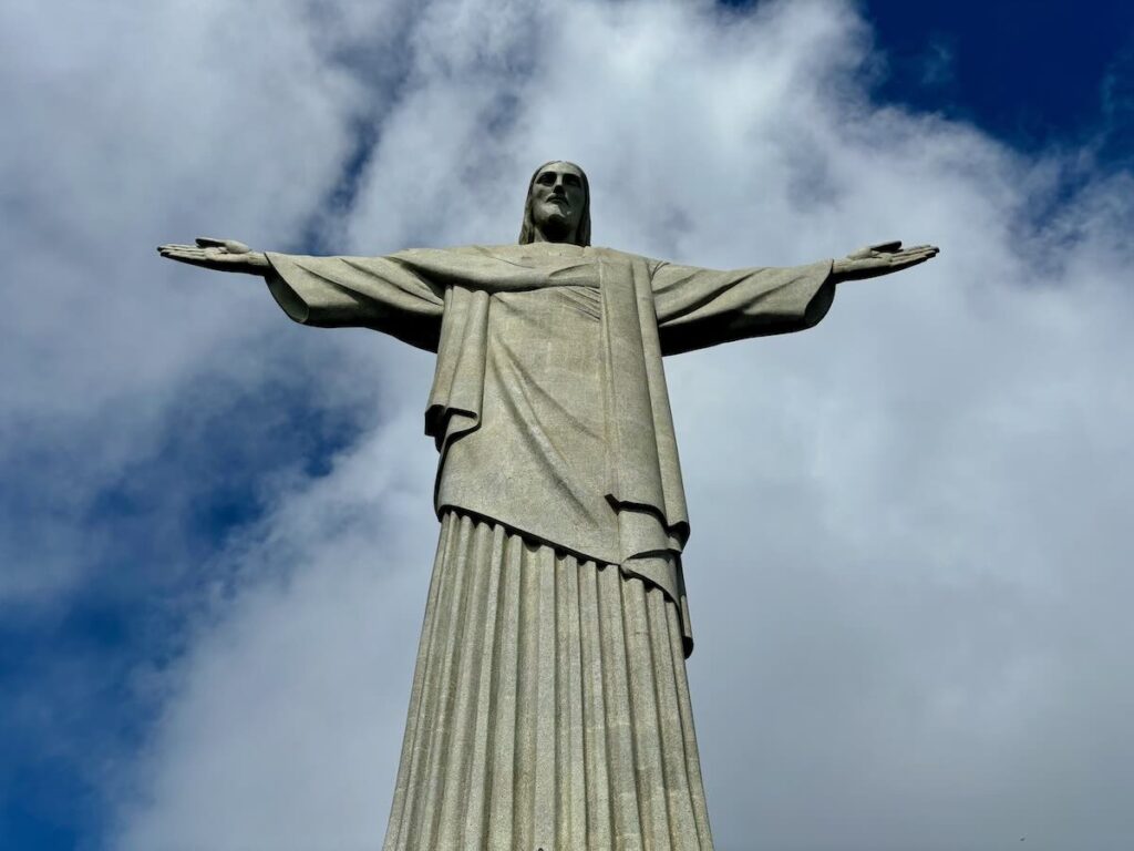Christ the Redeemer statue photographed from below, arms outstretched against blue sky and white clouds at Corcovado