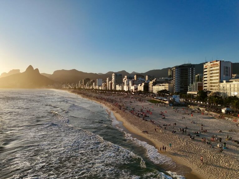 Ipanema Beach at sunset, busy crowds on the sand, Two Brothers Mountain silhouette and golden light along the shoreline