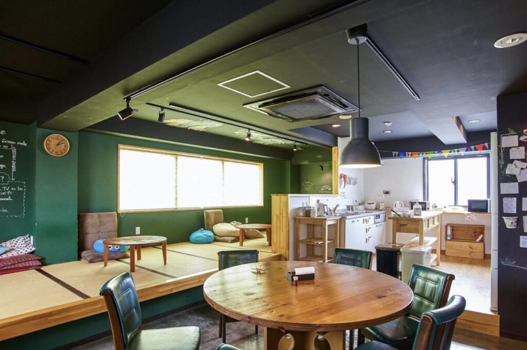 Communal lounge with tatami floor seating, round dining table and kitchen at Khaosan Tokyo Origami hostel