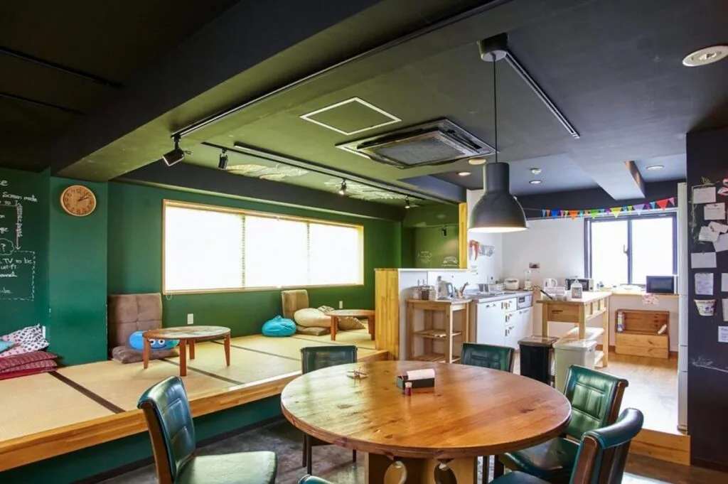 Communal lounge with tatami floor seating, round dining table and kitchen at Khaosan Tokyo Origami hostel