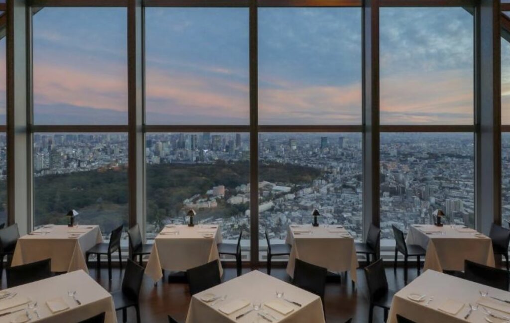 Dining tables by floor-to-ceiling windows at the New York Grill, Park Hyatt Tokyo, overlooking the city skyline at sunset
