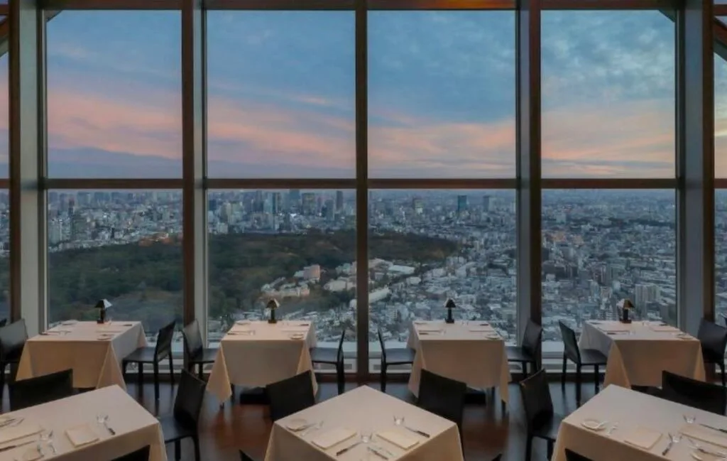 Dining tables by floor-to-ceiling windows at the New York Grill, Park Hyatt Tokyo, overlooking the city skyline at sunset