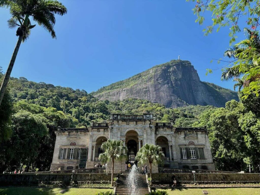 Parque Lage mansion, neoclassical 1920s building with palm trees and Christ the Redeemer visible on Corcovado in the background