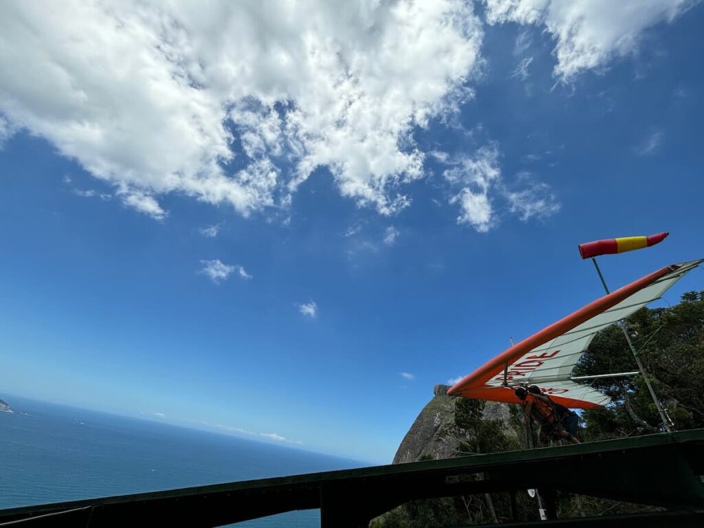Hang glider preparing to launch from the Pedra Bonita ramp, red and white sail, windsock and ocean view across São Conrado