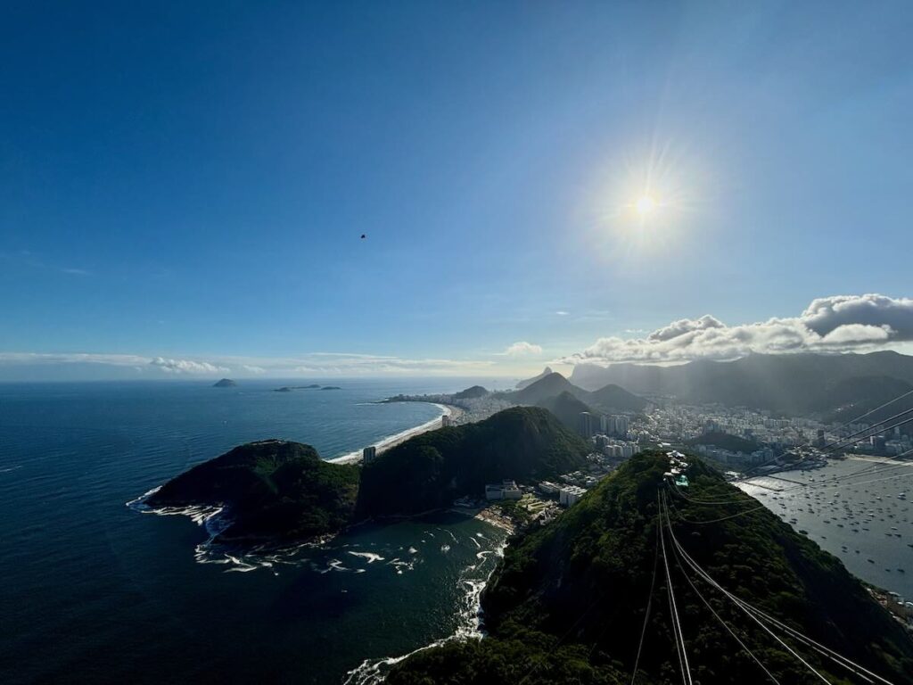 View from the top of Sugarloaf Mountain, cable car wires leading down to Urca, Copacabana coastline curving towards Two Brothers