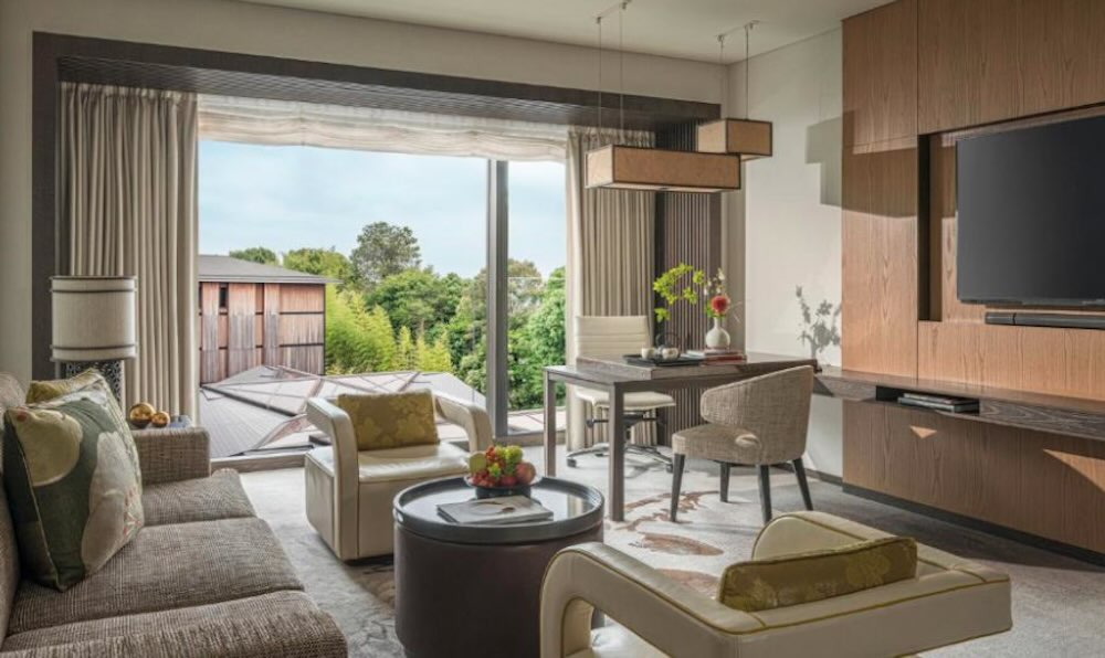 Four Seasons Kyoto suite with sofa, dining table and floor-to-ceiling windows looking onto the wooded garden and pond