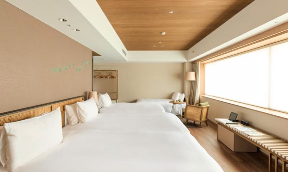 Family room with three beds pushed together, warm wood ceiling and a long window seat under a bright window