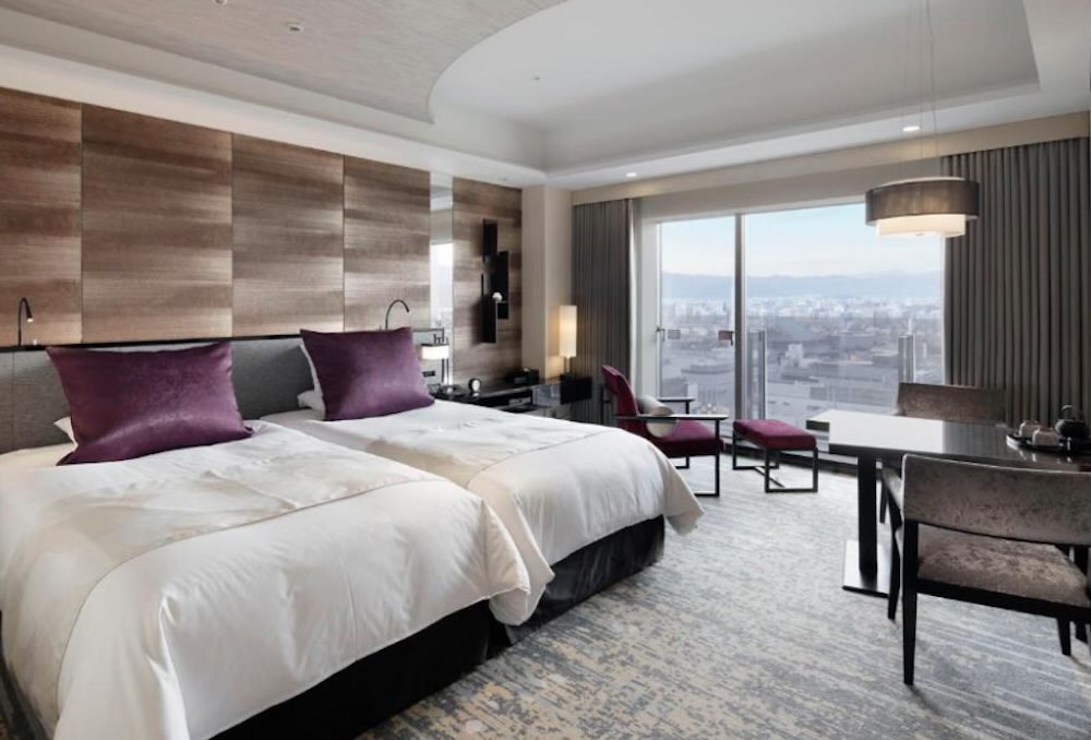 Granvia twin room with plush purple cushions, a work desk and big windows looking over the city to distant mountains