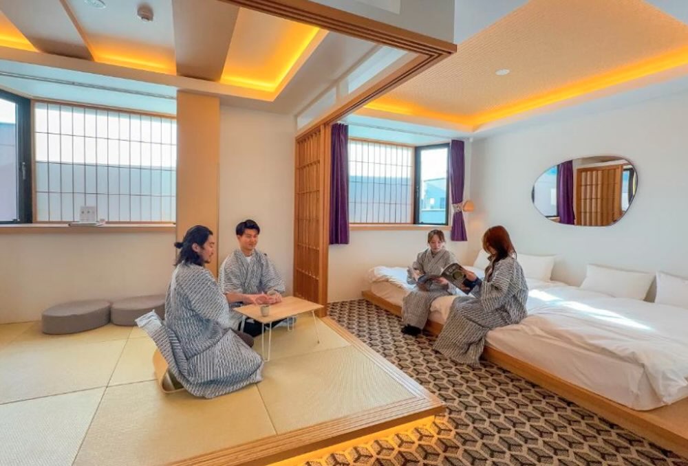Guests in yukata robes relaxing on tatami in a Japanese-style family room with low table, floor seating and a raised bed area