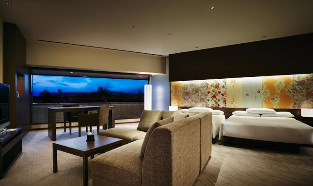 Hyatt Regency room at dusk with twin beds, a gold floral wall panel, sofa seating and a wide city-view window