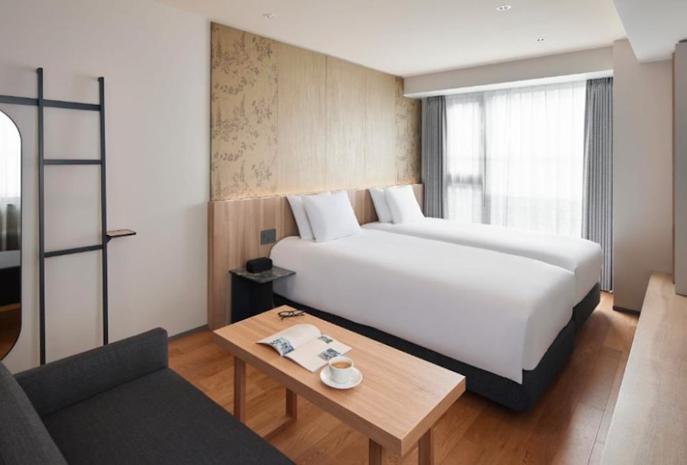 Oakwood Oike room with twin beds, a sofa and low table, floral wall panel and a kitchenette area for self-catering families