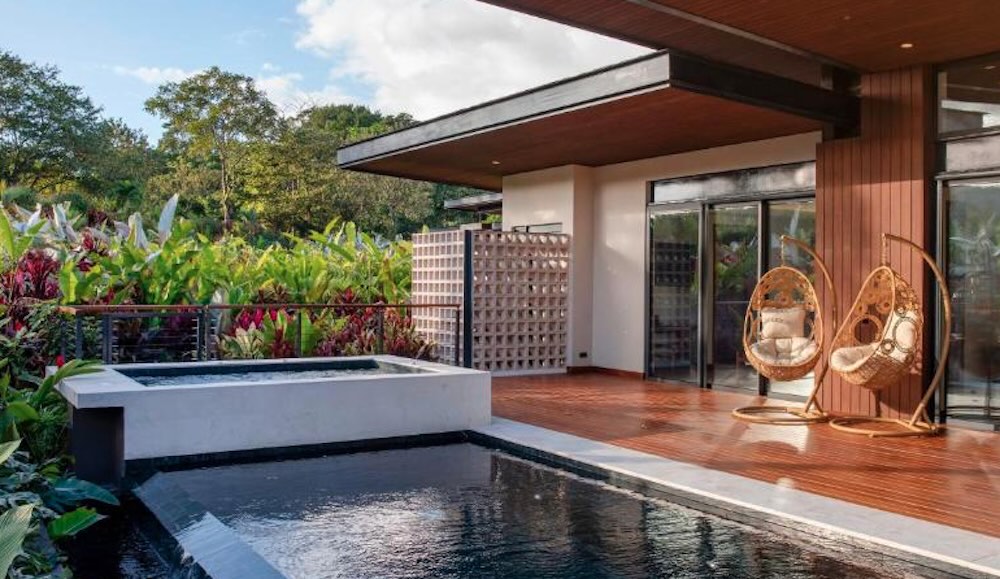 Private plunge pool and raised jacuzzi on a timber villa deck, with two hanging egg chairs and flowering planting alongside