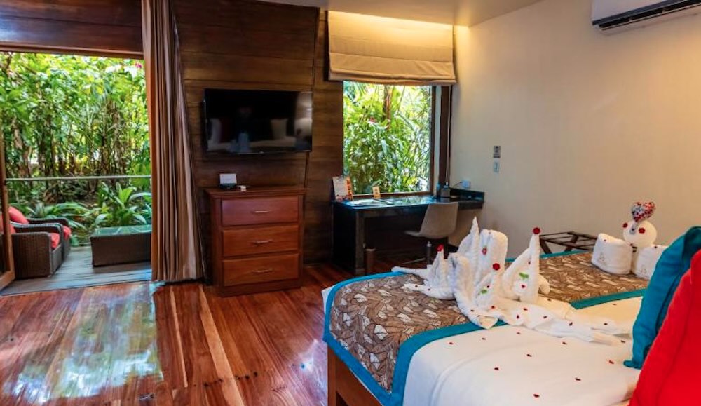 Hotel room with polished wood floors, towel swans folded on the bed and sliding doors opening onto a planted terrace