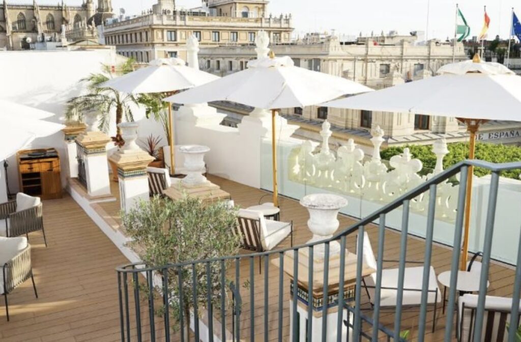White-parasol rooftop terrace with cushioned chairs and a record player, roofs of central Seville and the cathedral filling the background