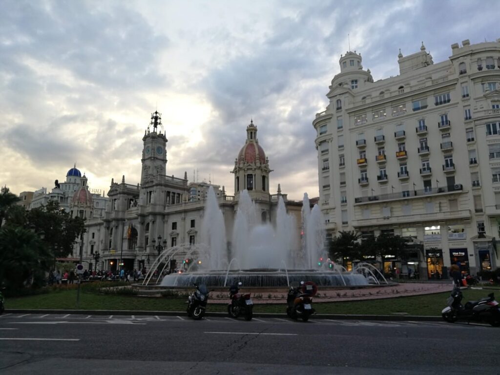 Plaza del Ayuntamiento in Valencia at dusk, its large central fountain in front of the ornate town hall building