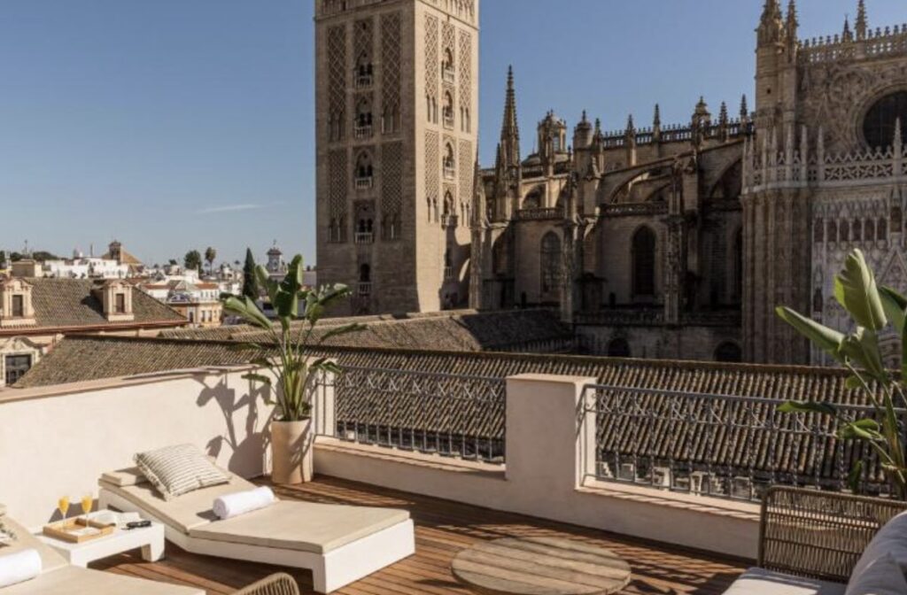 White cushioned loungers on a decked terrace facing Seville Cathedral and the Giralda up close, two glasses of cava on a low table in the sun