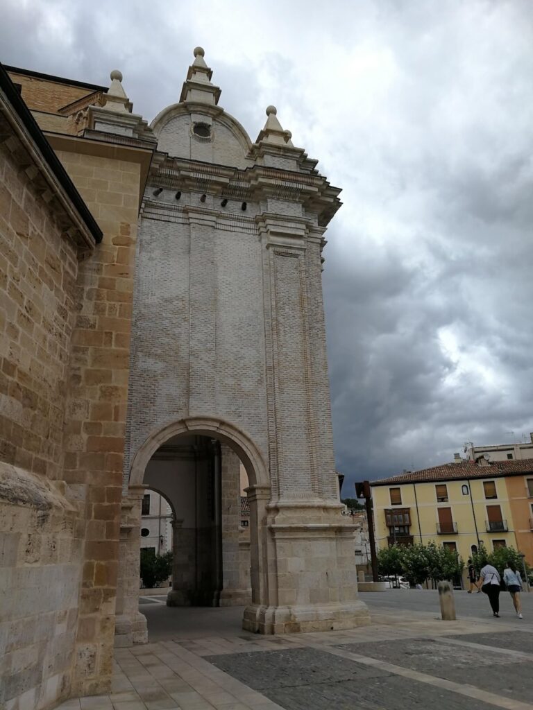 Tall brick-and-stone gateway tower beside Tarazona Cathedral, with the town square and houses under a stormy sky