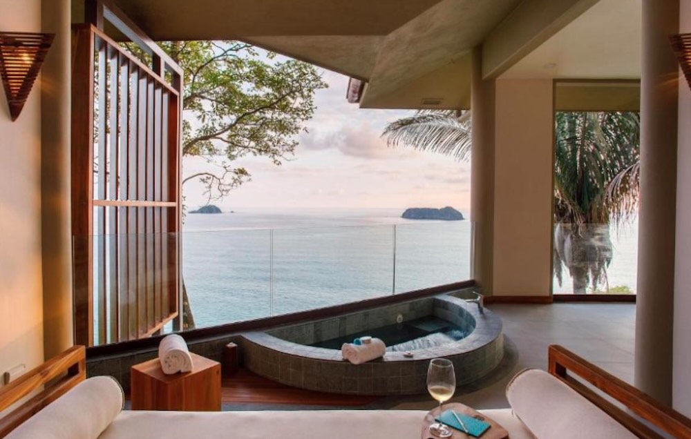 Private terrace with a sunken hot tub, sun loungers and a glass of wine, overlooking islands at sunset