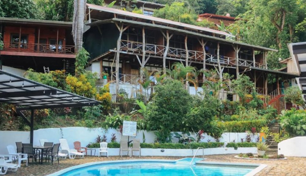Wooden jungle lodge on stilts built into a forested hillside, with a small pool and shaded seating in the foreground