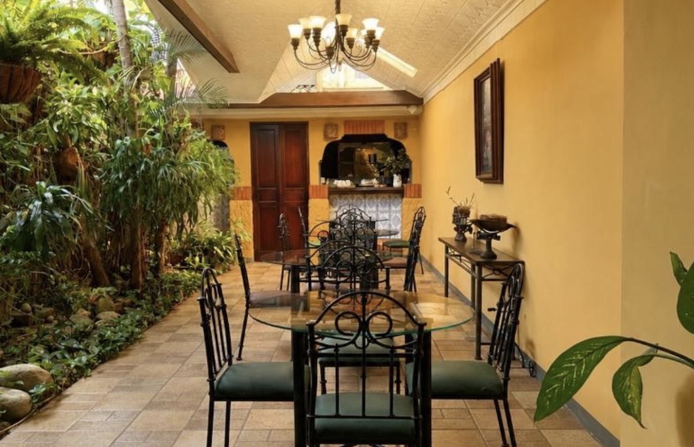 Indoor courtyard breakfast area with glass-topped tables, wrought iron chairs, yellow walls, a chandelier and a planted bed running alongside