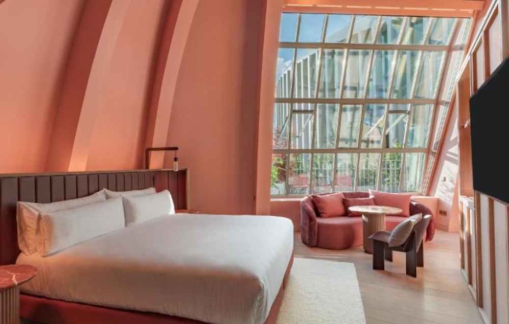 Coral pink room with curved walls following the old dome, a large angled glass window and a rounded sofa and table set into the corner.