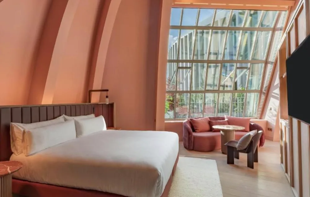 Coral pink room with curved walls following the old dome, a large angled glass window and a rounded sofa and table set into the corner.