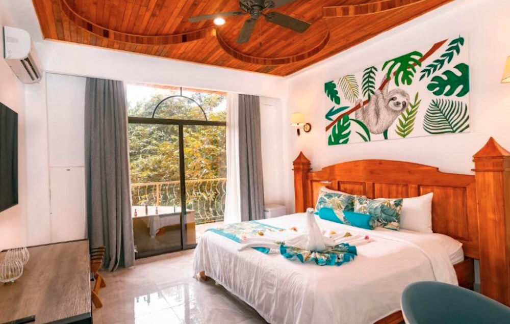 Bedroom with a painted sloth mural above the bed, a curved wooden ceiling and glass doors onto a leafy balcony