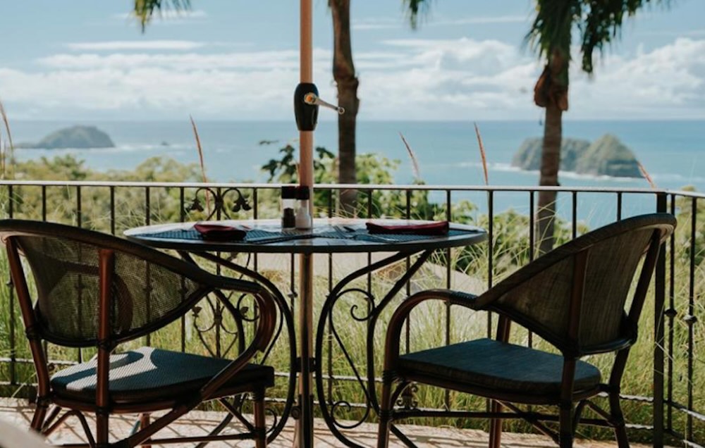 Table for two on a terrace with a parasol, looking out over the ocean to two forested islands