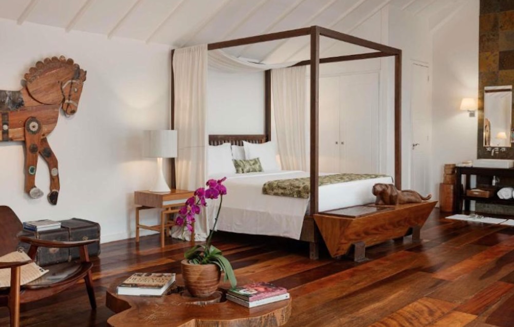 Four-poster wooden bed under a white beamed ceiling, with dark polished floorboards, a carved wooden horse on the wall and an orchid on a low table