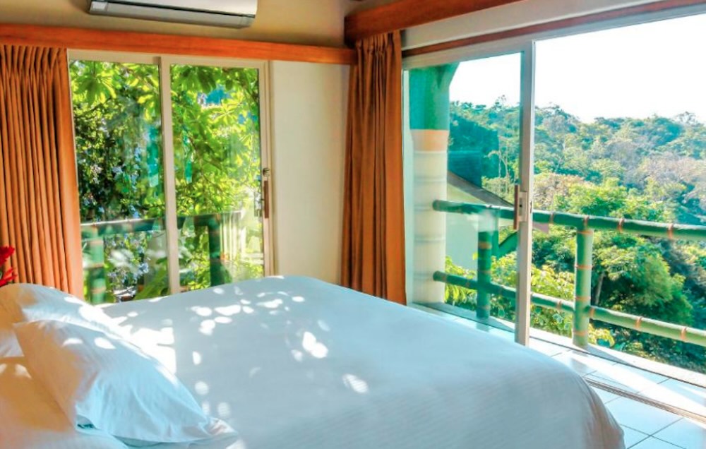 Bed beside floor-to-ceiling sliding doors opening onto a green bamboo balcony rail and thick jungle