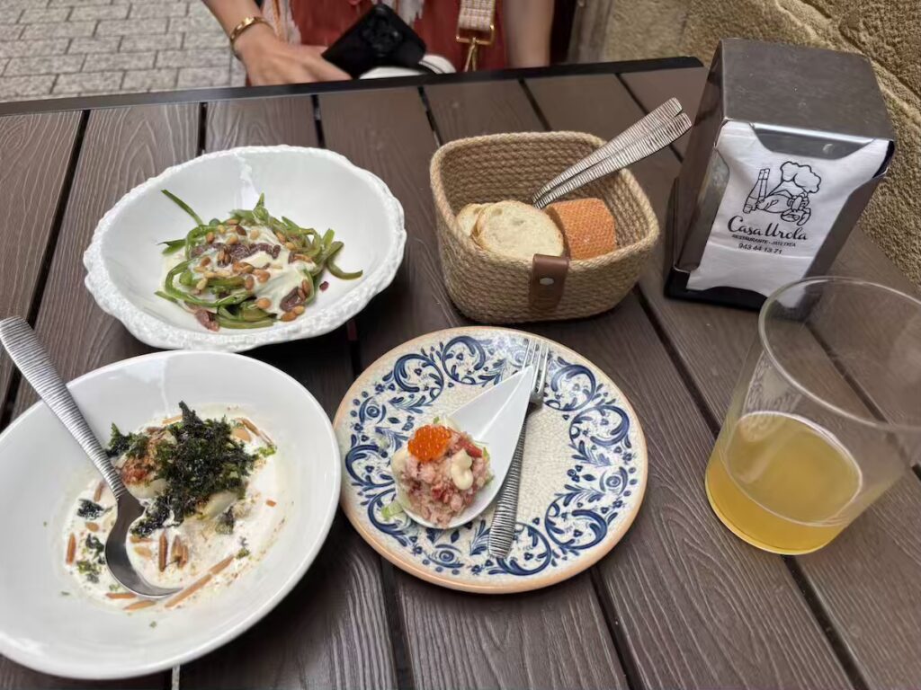 Three pintxos, a bread basket and a glass of cider on an outdoor table at Casa Urola pintxo bar in San Sebastián