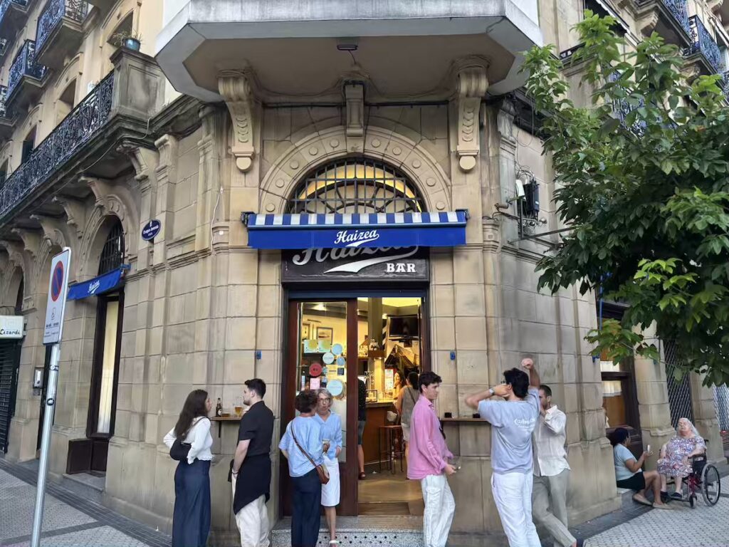 Bar Haizea on a street corner, blue awning above the door and people standing outside with drinks