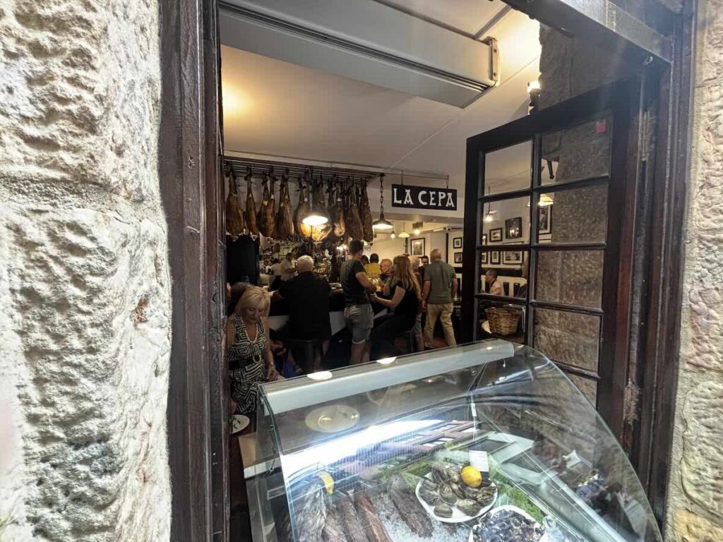 Looking into La Cepa through the doorway, hams hanging over the bar and an oyster display in the window