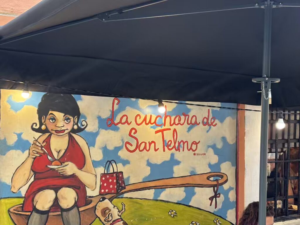 Painted mural of a woman sitting in a giant spoon on the wall outside La Cuchara de San Telmo pintxo bar in San Sebastián old town