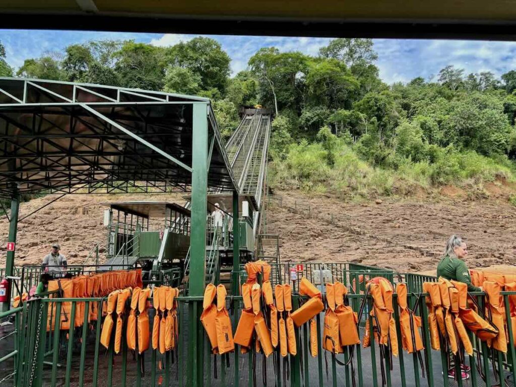 Rows of orange life jackets hanging on railings at a boarding deck, with a funicular track climbing the hillside behind.