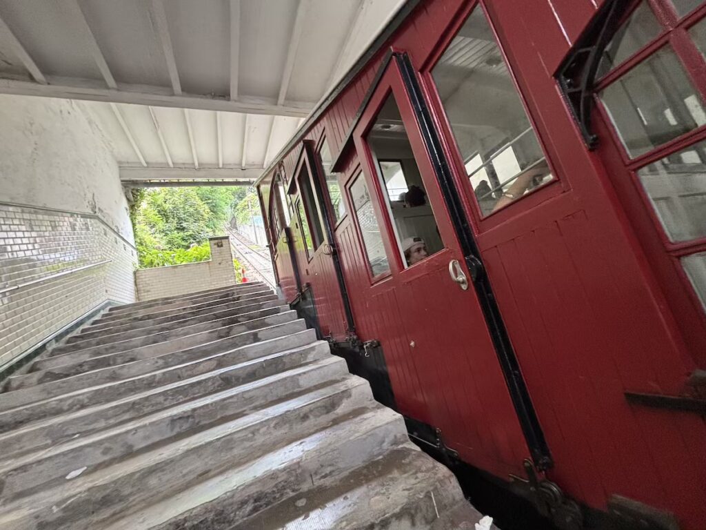 A dark red wooden funicular carriage with black-framed windows waiting alongside a flight of worn stone steps under a covered platform.