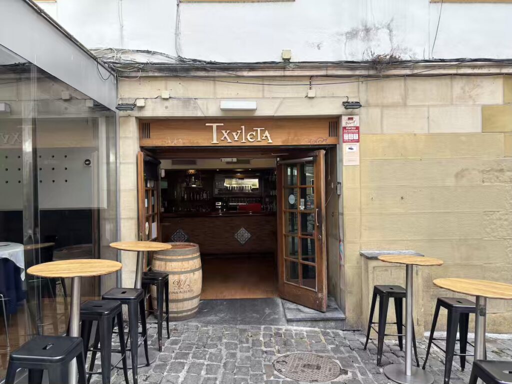 Entrance to Txuleta bar, with a wine barrel and high stools on the cobbles outside