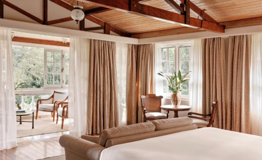 Colonial-style room with a pitched beamed ceiling, tall curtained windows and doors onto a balcony with cane chairs